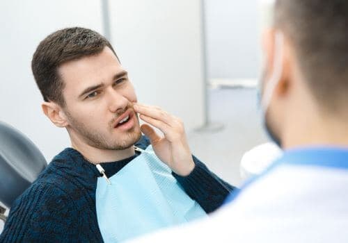 Man in a dental chair wincing from pain from a tooth infection.