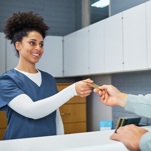 Woman in blue scrubs handing payment card back to man at counter