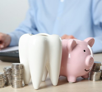 A ceramic model of a tooth, a piggy bank, and coins on a wooden table
