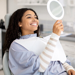 woman smiling at reflection in handheld mirror
