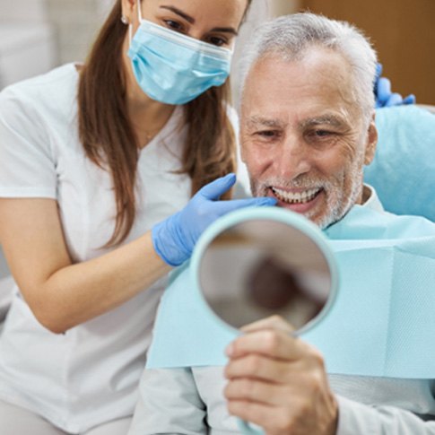 older dental patient looking in mirror and smiling  