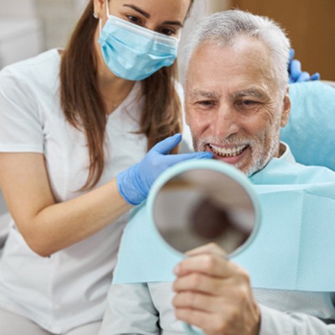 older dental patient looking in mirror and smiling