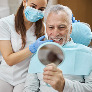 Senior man in dental chair admiring his smile in a mirror