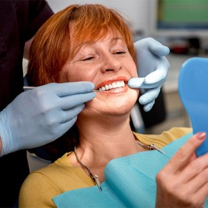 A senior woman looking at her new dental implants in a hand mirror