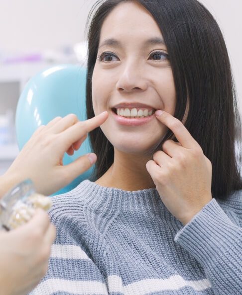 Woman pointing to smile after tooth replacement with dental implants