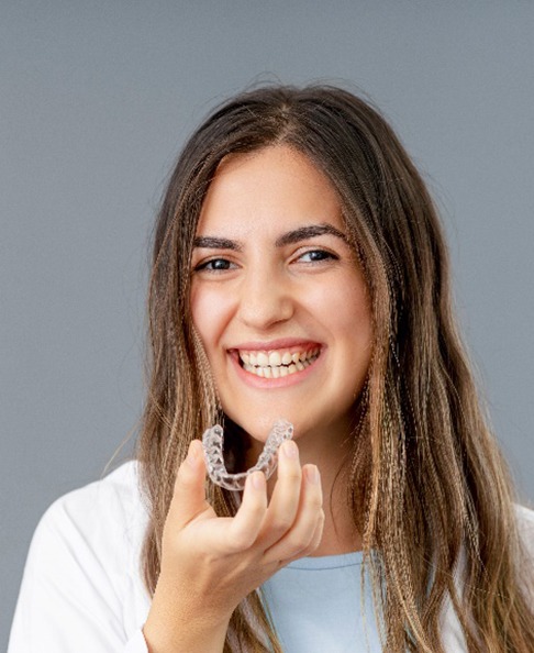 Young woman smiling while holding Invisalign in San Antonio