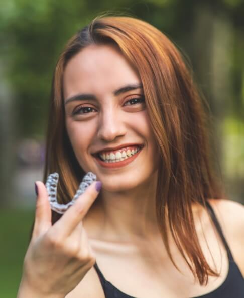 Smiling woman holding clear braces orthodontics tray