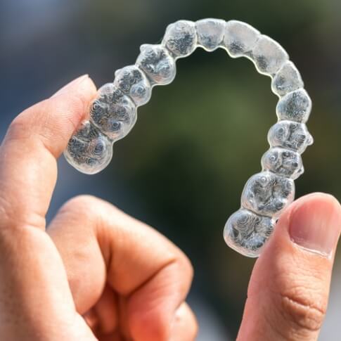 Hand holding an Invisalign clear aligner tray