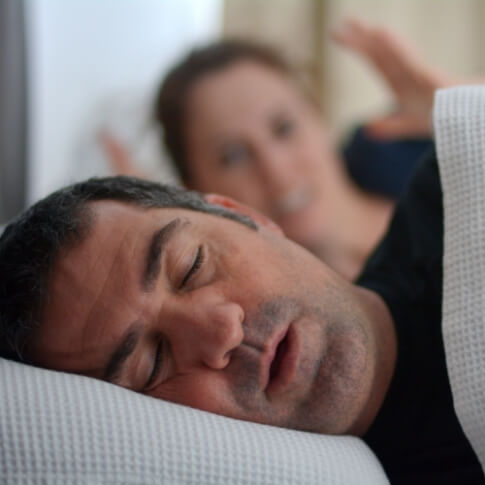 Frustrated woman in bed with snoring man who needs sleep apnea treatment