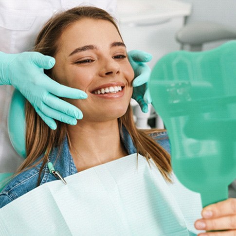 Dentist showing patient their smile in the reflection of handheld mirror