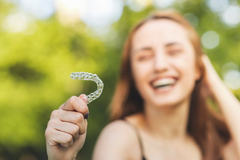 smiling young woman holding her Invisalign aligner
